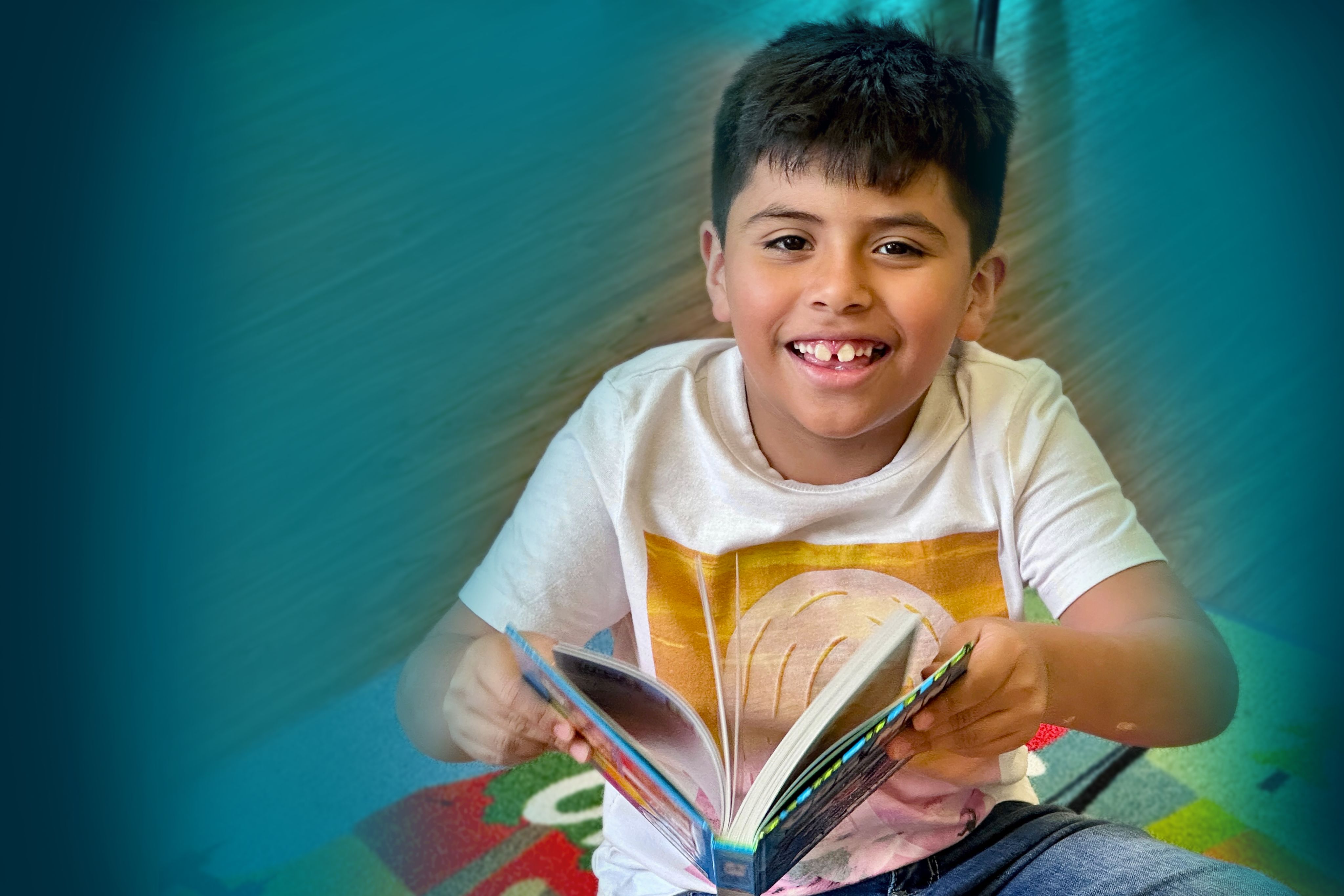 A young boy smiles and holds an open book. The image has a teal gradient around the boy.