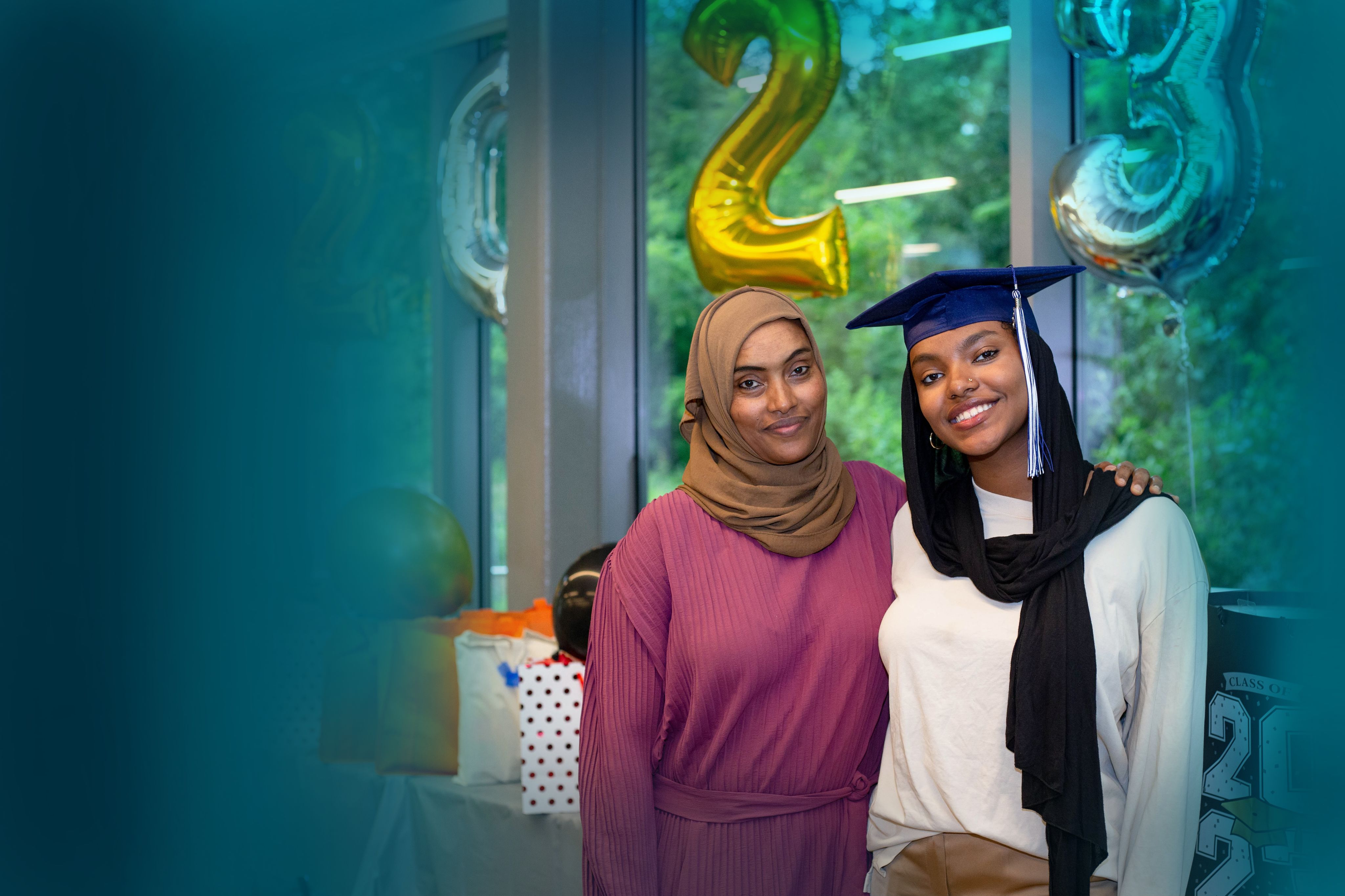 A mother and daughter smile for a photo at an AHC graduation celebration. The edges of the photo have a teal gradient.