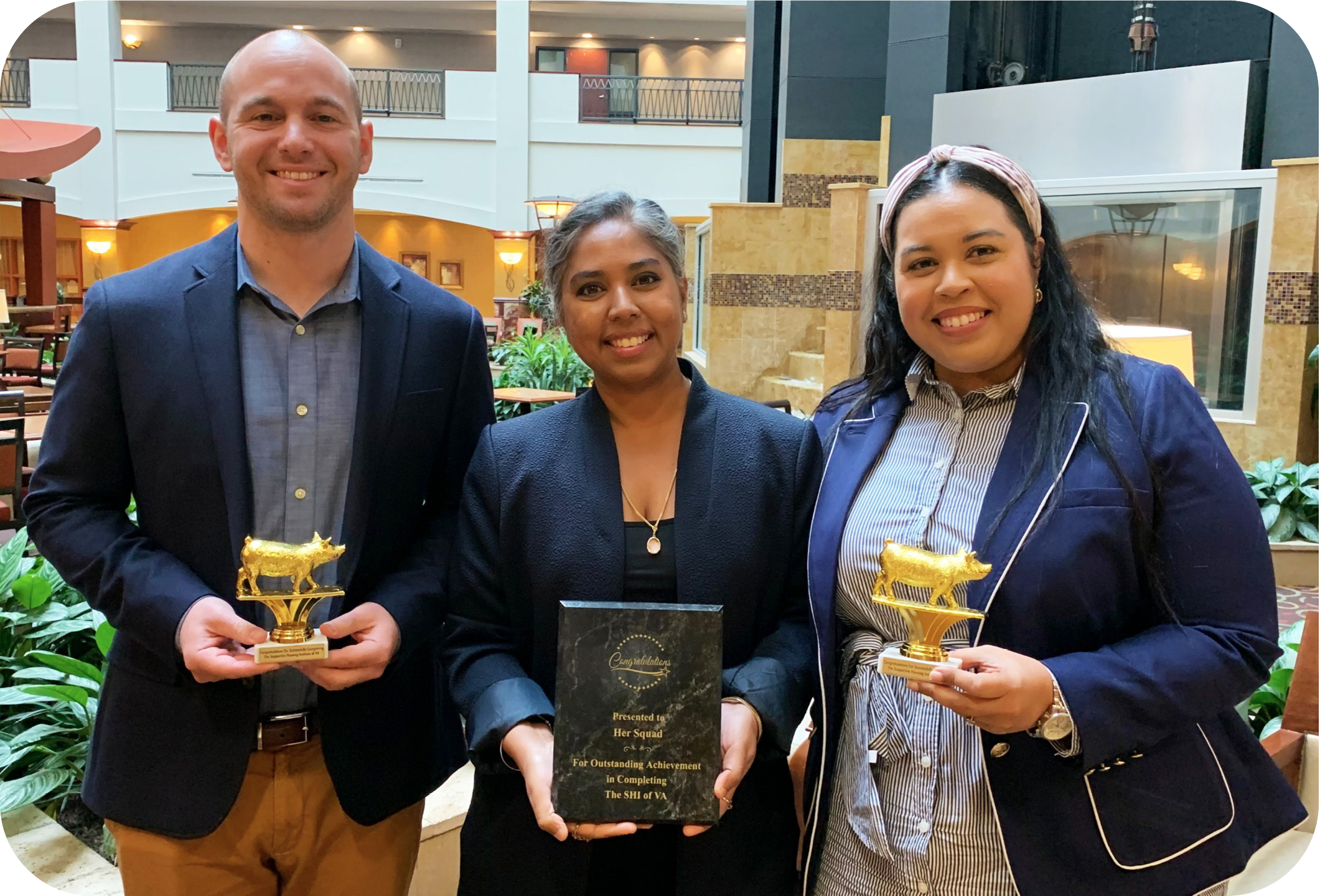 Image of three adults (one man and two women) smiling and holding plaques and awards.